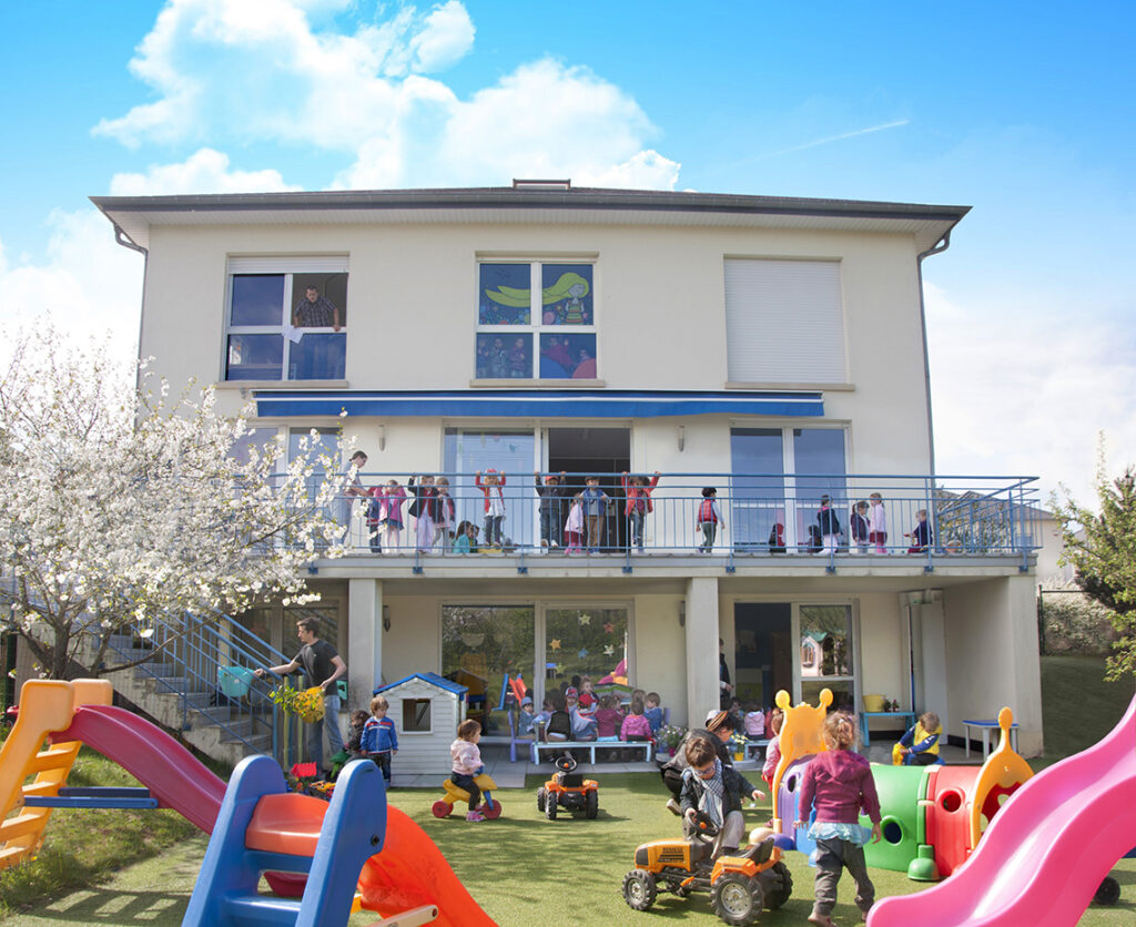 Jardin et façade arrière de la crèche Les P'tits Malins de Strassen avec des enfants qui jouent