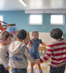 Enfants qui font une ronde avec un musicien qui joue de la guitare